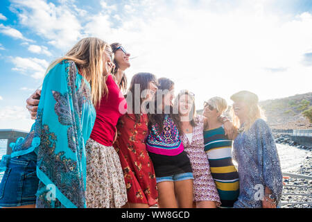 group of seven nice and beautiful caucasian girls young women have fun and laugh and smiles outdoor near the ocean during the sunset, backlight people enjoying the outdoor leisure activity together Stock Photo