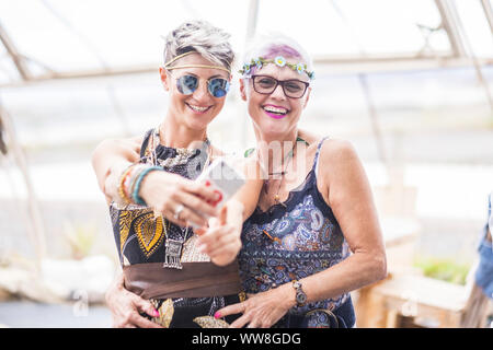 hippy couple of caucasian beautiful females use a smart phone, Different ages nice attractive people stay together in happy leisure activity with friendship, Sharing content on social for cheerful old and young ladies Stock Photo