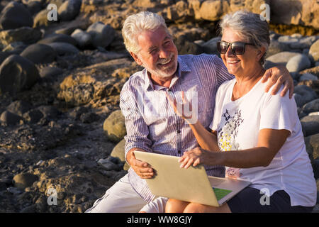 concept of vacation, technology, tourism, travel and people - happy senior couple with tablet pc computer on pebble beach laughing and joking, White hair Stock Photo