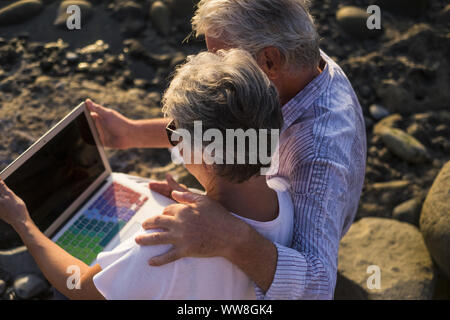 concept of vacation, technology, tourism, travel and people - happy senior couple with tablet pc computer on pebble beach, White hair Stock Photo