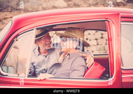 Nice beautiful couple of senior adult people inside an old red vintage car enjoy and stay together in outdoor travel leisure activity. Married and forever together life. traveling concept with happiness Stock Photo