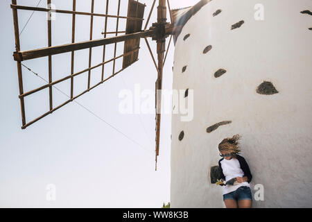 nice beautiful cheerful lady with blonde curly hair standing under a windmill in outdoor scenic place reading a book and enjoying the leisure activity.  happy lifestyle concept for people smile Stock Photo