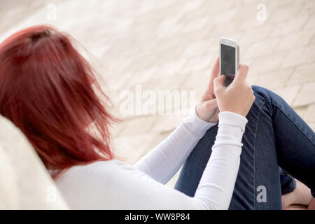Pretty smiling redhead woman sending messages on her cell phone in a park. . Focus on her phone Stock Photo