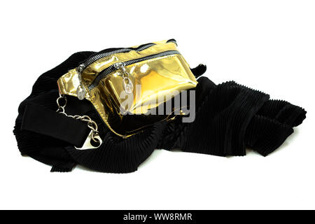 Gold shiny travel belt bag for women on a black velvet scarf isolated on white. Belt bag has chain strap. Stock Photo