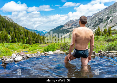 Hot springs on Conundrum Creek Trail in Aspen, Colorado in 2019 summer with man in swimsuit looking at valley view Stock Photo