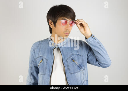 Young Asian Man in Jeans Jacket or Denim Jacket Touching Red Glasses. Denim or Jeans Jacket Men Fashion on Gray Background Stock Photo