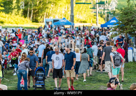 Aspen, USA - July 4, 2019: Snowmass village town and many people crowd on ski slope listening to free concert with lift cable cars Stock Photo