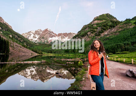 Maroon Bells in Aspen, Colorado at blue hour in July 2019 summer and moon reflection at sunrise with woman drinking coffee or tea in morning Stock Photo