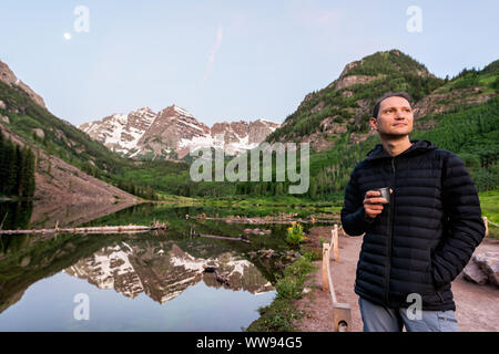 Maroon Bells lake in Aspen, Colorado at blue hour in July 2019 summer and moon reflection at sunrise with man drinking coffee or tea in morning Stock Photo