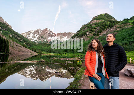 Maroon Bells with woman and man couple in morning in Aspen, Colorado at blue hour in July 2019 summer and moon reflection at sunrise Stock Photo
