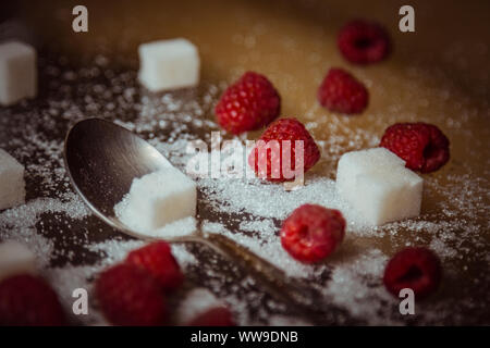 berries of red raspberries with a teaspoon and cubes of refined sugar lie on a wooden rustic table top view. Stock Photo