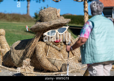 13 September 2019, Baden-Wuerttemberg, Höchenschwand: A tourist stands in front of a 'Miss Bikini' made of straw at the 10th Höchenschwander Straw Sculpture Competition. Photo: Patrick Seeger/dpa Stock Photo