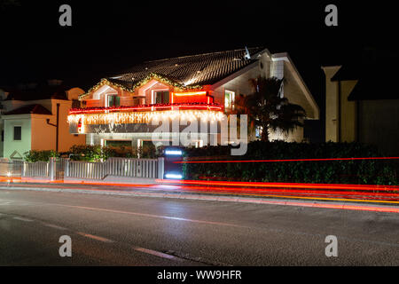 House with Christmas illumination. On the road going car, leaving traces of light. Long exposure. Stock Photo