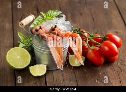 Raw langoustine in a bucket with vegetables and herbs on wood Stock Photo