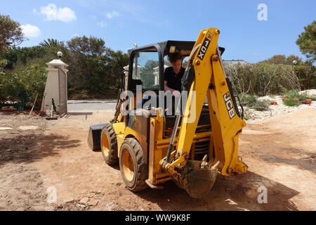 Algarve, Portugal 10 April 2019: A JCB mini digger being used to do landscaping work in a front garden Stock Photo