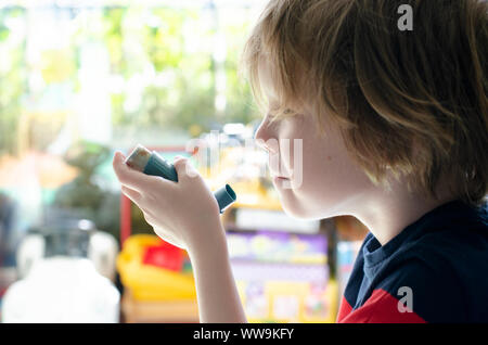 United Kingdom, 10 July 2019: Little boy in front of a window using a Ventolin inhaler Stock Photo