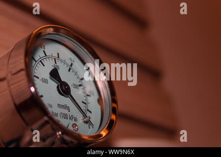 Close up of a pressure gauge indicating level zero, mounted on a wall, elegantly made case, white face and black needle.. Stock Photo