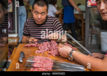 Xian, China -  July 2019 : Two men preparing sticks with pork and beef meat for kebabs to sell on the street in the Muslim Quarter Stock Photo