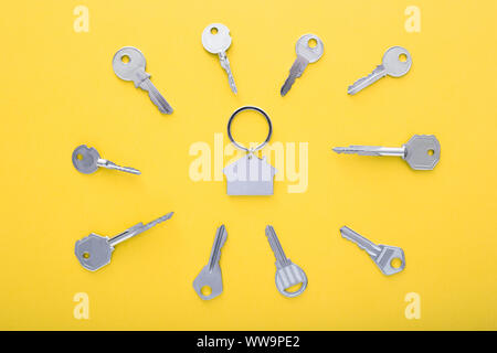 Keys and trinket in shape of house in the center on color background, top view. Stock Photo