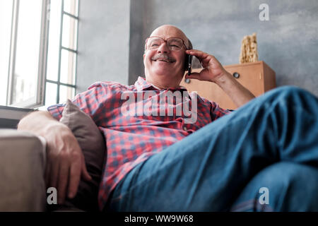 Retired hispanic man talking on phone sitting at living room and laughing. Discuss important questions. Stock Photo