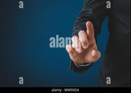 Businessman touching blank virtual screen with his finger. Over navy blue background with copy space. Stock Photo