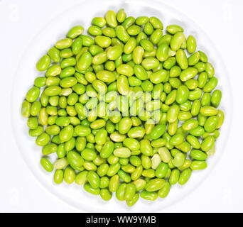 Edamame. Green soybeans on a white plate. Mukimame, unripe soya beans outside the pod. Glycine max, a legume, edible after cooking and protein source. Stock Photo