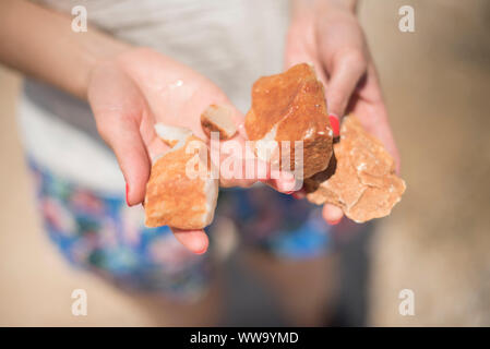 Naxos, Greece - June 28, 2018: A visitor holds orange rocks found on the beach at Alykó, on the southwestern shore of the island of Naxos. Stock Photo