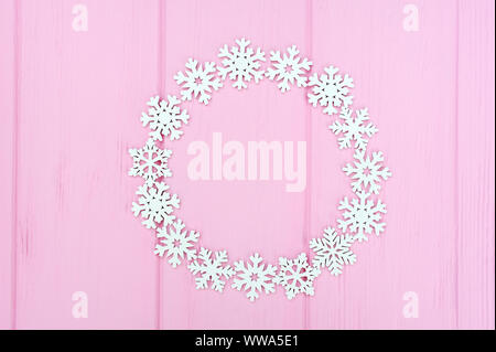 Holiday round frame made of christmas white snowflakes on pink wooden background. Composition with place for text. Flat lay, top view Stock Photo