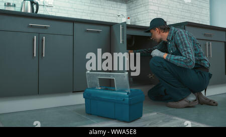 Portrait of mature handyman wearing uniform checking water pipes in the kitchen. Horizontal shot Stock Photo