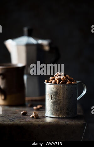 Coffee beans in a tin measuring cup against dark rustic background. Low key with shallow depth of field Stock Photo