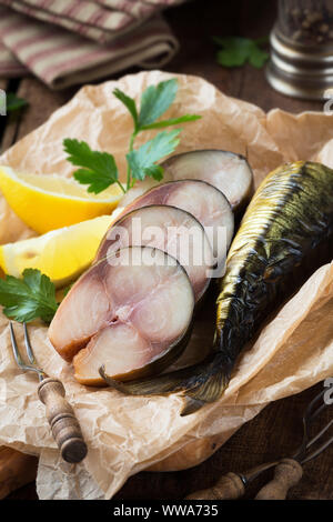 Cold smoked mackerel fish cut in slices and served on a parchment paper with fresh parsley leaves and lemon wedges Stock Photo