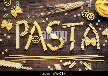 Variety of types and shapes of dry Italian pasta concept. Pasta word made of fusilli, spaghetti, penne, conchiglie, farfalle and ruote Stock Photo