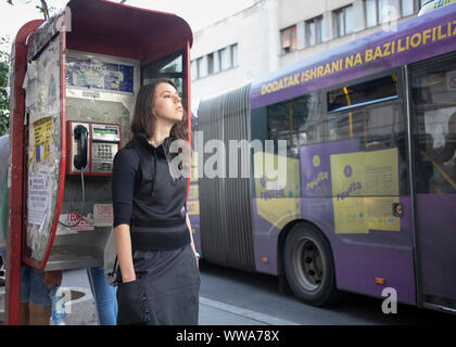 Belgrade, Serbia, September 10th 2019: Young woman standing on the sidewalk leaning against a pay phone at Glavna Street in Zemun Stock Photo