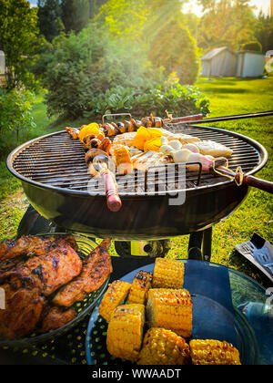 Assorted delicious grilled meat and vegetables over coal barbecue grill in sunny green garden. Stock Photo