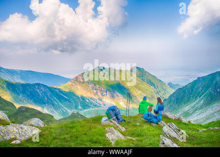 Back shot of young couple sitting down in the mountains on edge of cliff, admiring the view Stock Photo