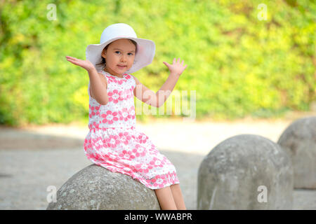 Adorable little girl wearing white hat sitting on stairs on warm and sunny summer day Stock Photo