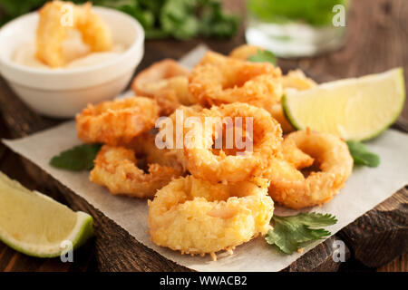 Fried squid rings on wooden cutting board with lemon and parsley Stock Photo