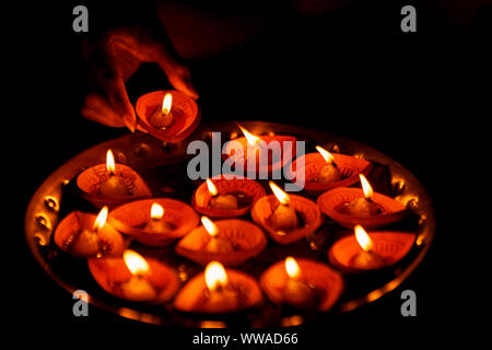 Indian woman or girl holding lit traditional clay diya or oil lamp with a thali or plate full of diya for decoration on Diwali night. Stock Photo