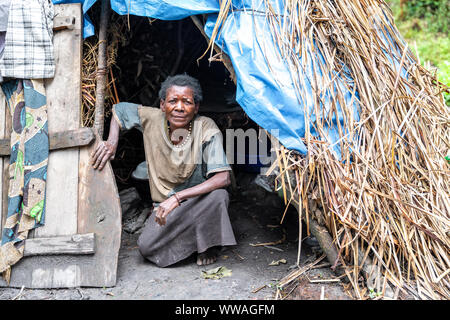 Portrait of pygmy tribeswoman crouching in front of primitive hut, Uganda Stock Photo