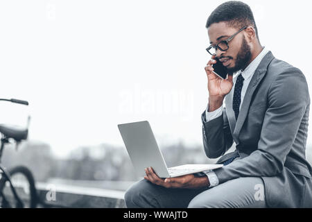 Confident businessman talking on phone and using laptop Stock Photo