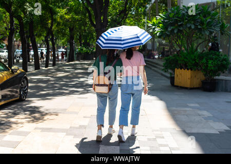 A fashionable area of Beijing where young girls stroll. Chinese girls walk with an umbrella protecting themselves from the sun's rays. Stock Photo