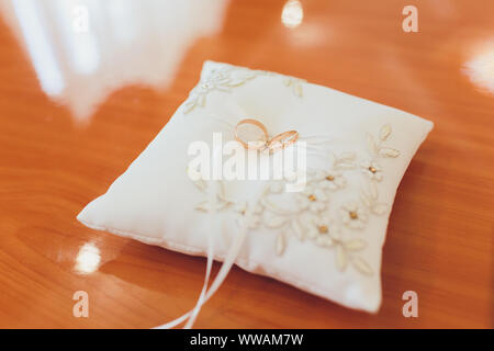 Two wedding gold rings lying on silk lace cushion for rings. Wedding accessories bride and groom before the ceremony photographed on a white backgroun Stock Photo