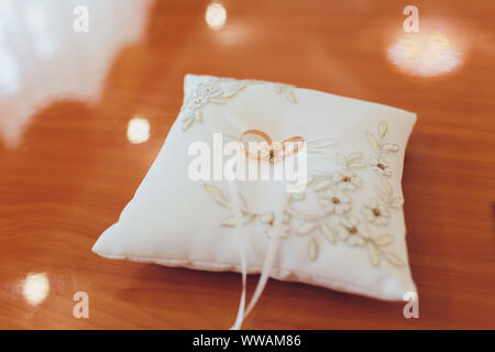 Two wedding gold rings lying on silk lace cushion for rings. Wedding accessories bride and groom before the ceremony photographed on a white backgroun Stock Photo