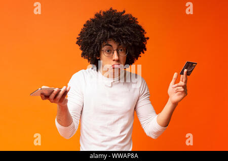 Upset black man holding bank card and smartphone Stock Photo