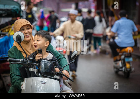 Xian, China -  July 2019 : Muslim woman with her son sitting on a scooter on the road in the Muslim Quarter Stock Photo