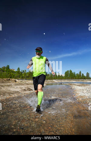Man with grey beard running on the river with splashes in the morning. Healthy lifestyle concept Stock Photo