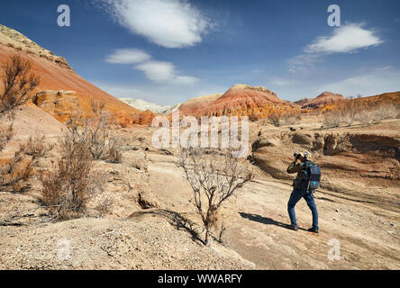 Tourist with backpack and camera taking a picture at the dusty canyon on surreal red mountains against blue sky in the desert Stock Photo