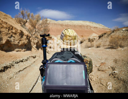 Tourist with backpack and solar panel in canyon on surreal red mountains against blue sky in the desert Stock Photo
