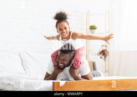 Cheerful african girl playing with father, flying like plane Stock Photo