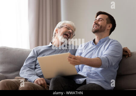 Happy old father and young son laughing using laptop together Stock Photo